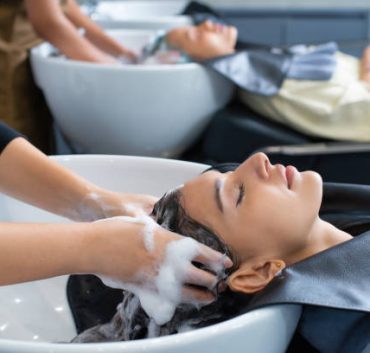 Young woman in hairdresser salon during hair wash after haircut. Woman applying shampoo and massaging hair of a customer. Female having her hair washed in a hairdressing salon.